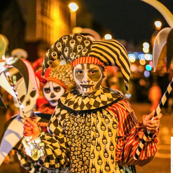 Children in vibrant jester costumes with skull face paint take part in the lively Derry Halloween parade
