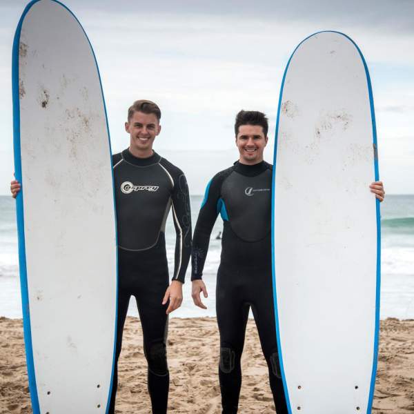 Two surfers pose with their boards in front of the sea Whiterocks Beach, Portrush, County Antri