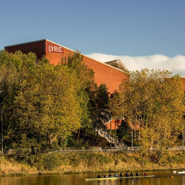 Exterior of The Lyric Theatre in Belfast on a sunny day with rowers on the river beside it