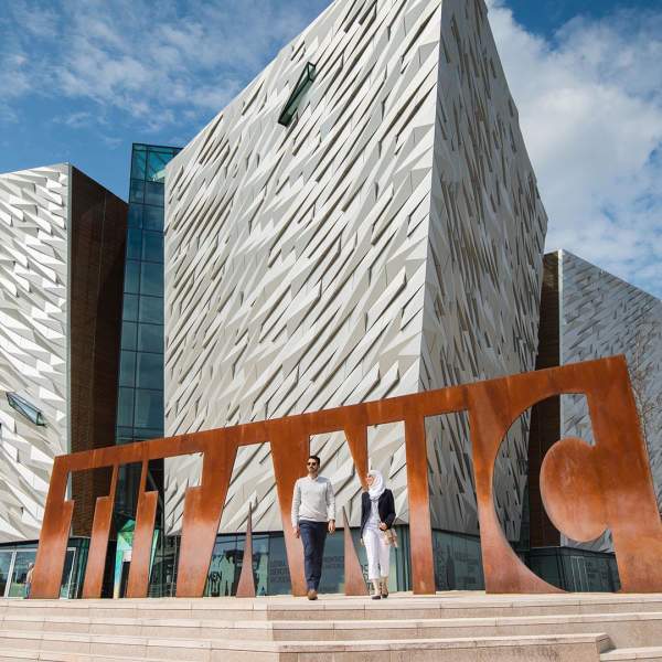 External Image of a couple visiting Titanic Belfast, at the Titanic Belfast sign.