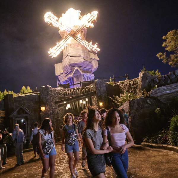 Theme park guests walk out of The Burning Blade Tavern as the windmill bursts into flames at Universal Epic Universe