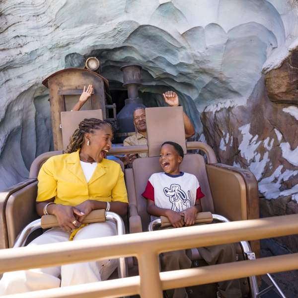 A mother and son laughing on Expedition Everest at Disney's Animal Kingdom Theme Park, A roller coaster train exits an icy mountain tunnel decorated with carved rock and snow textures from Expedition Everest at Disney’s Animal Kingdom, with riders seated in rows and visible track supports behind.
