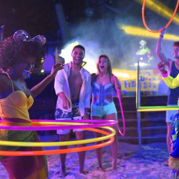 Water park visitors watch a glowing hula hoop competition in amazement. One woman wears sparkling mouse ears.