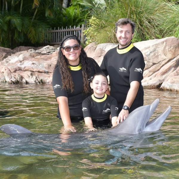 Jocelyn Aranda and her family smile with a dolphin during the Dolphin Swim experience at Discovery Cove