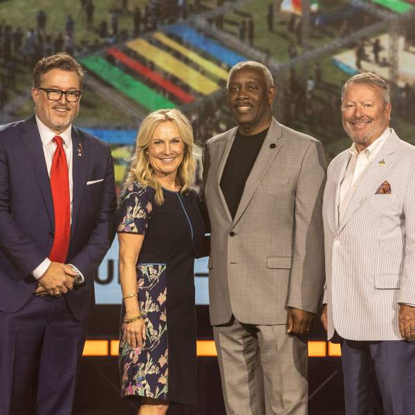 Four presenters stand side by side on stage posing for a photo beneath a large scenic backdrop.