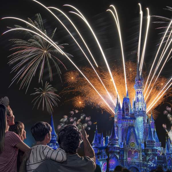 Two adults and two children watch spectacular fireworks over Cinderella Castle at Magic Kingdom Park