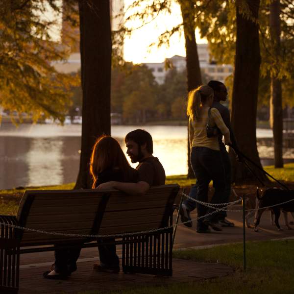 A couple sitting on a park bench and another couple walking their dog along Lake Eola
