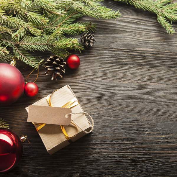 Christmas tree branches with gift box, ornaments and pine cones on a wooden background