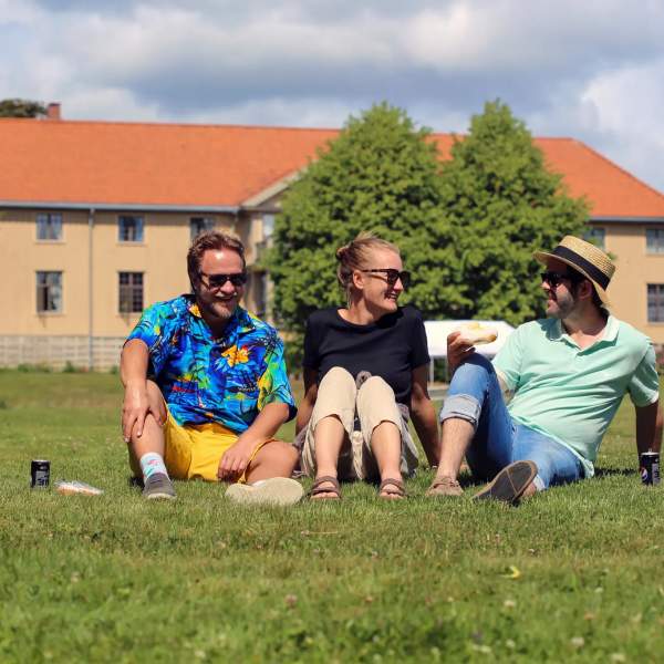 En kvinne og to menn slapper av i gresset foran et museum