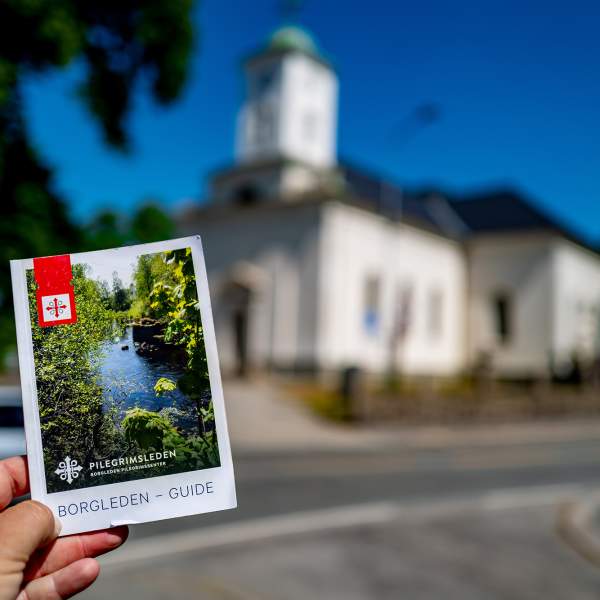 En hånd holder i en brosjyre for Borgleden foran en kirke