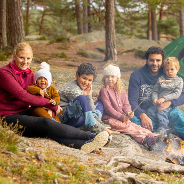 En familie på seks som sitter rundt bålet og griller pølser. Foto.