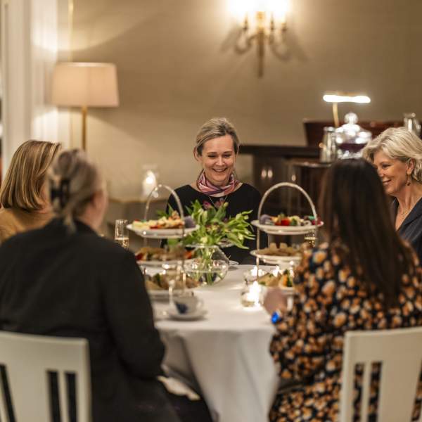 En gruppe damer som sitter rundt et dekket bord på Borregaard Hovedgård og har afternoon tea.