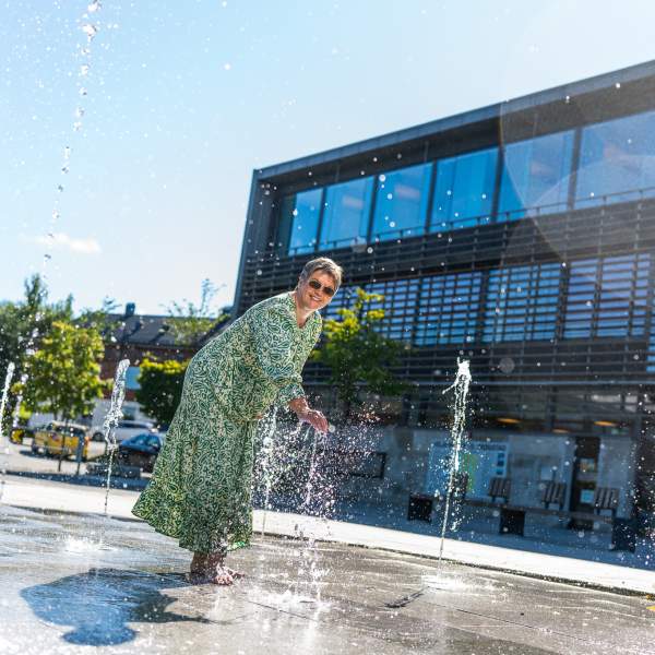 En dame som leker seg i fontenen på Skjønhaug torg
