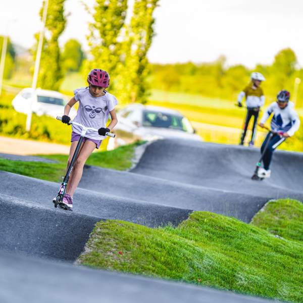 Tre barn på sparkesykkel i pumptrackbanen med bølgete asfalt