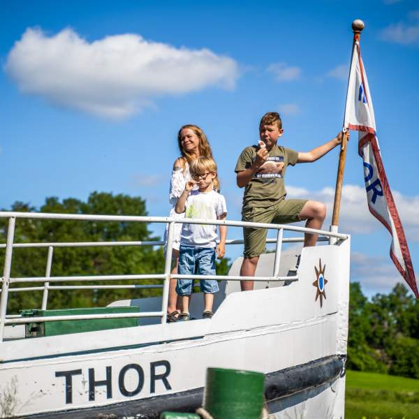 En dame og to barn står i baugen av båten Thor