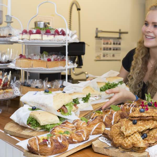 En disk full av bakevarer og en blid ung dame bak disken