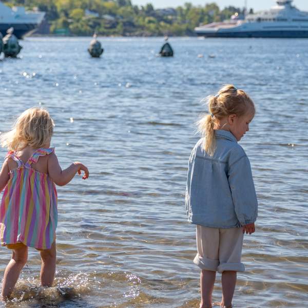 To små jenter i strandkanten på Sjøbadet, med Bastøfergen i bakgrunn