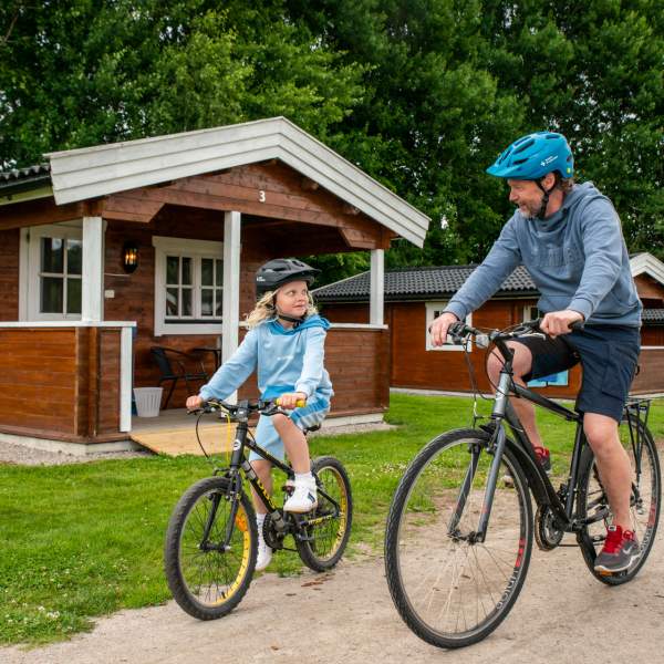 En mann og en jente på sykkel foran en camping hytte.