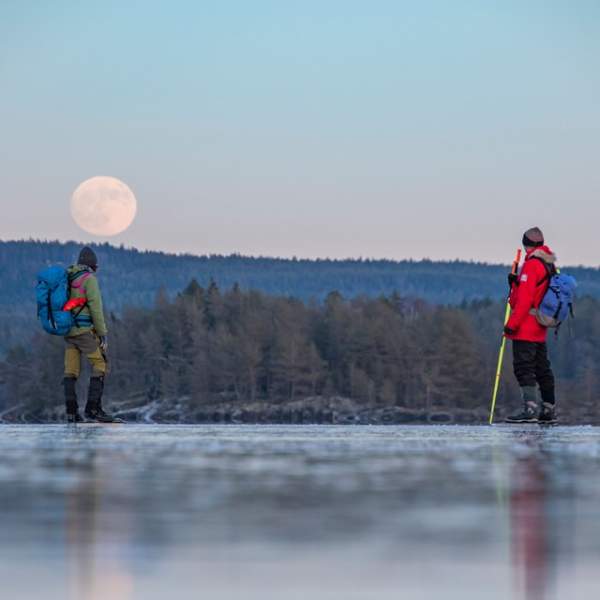 To menn på turskøyting med vakker måne på åskammen