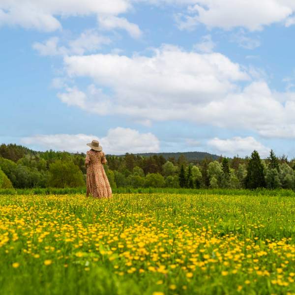 Kvinne i kjole som står i en blomstrende sommereng.