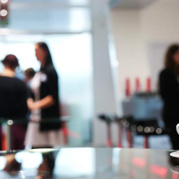 A photograph showing a cup and saucer in the foreground, with people in smart clothes in the background at a conference event
