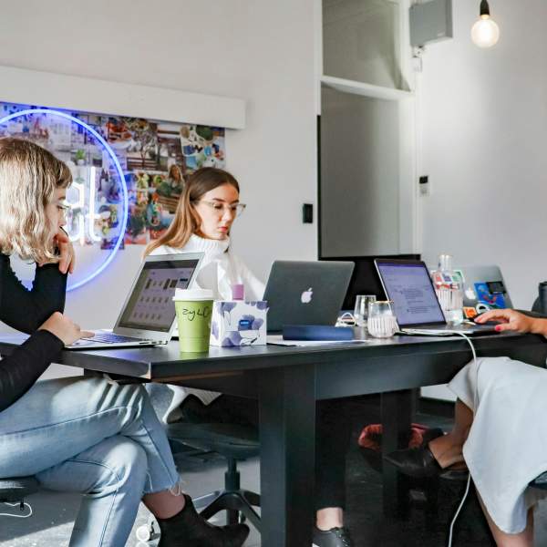Three women work on their laptops while seated at the same table.