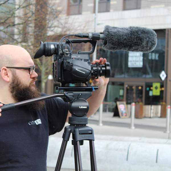 A person stood behind a camera filming in Guildhall Square