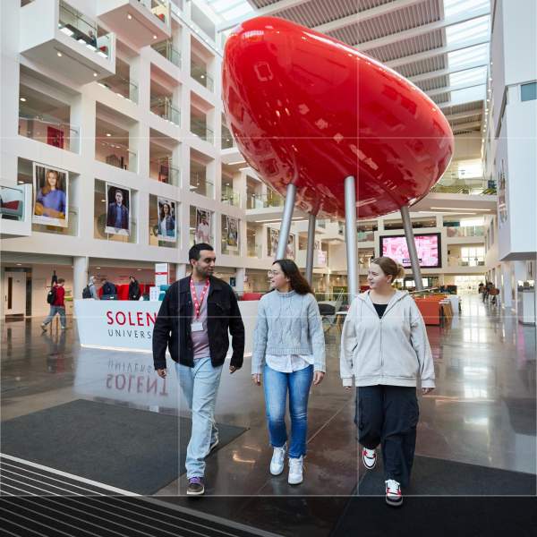 Three people walking towards the camera inside The Spark building at Southampton Solent University