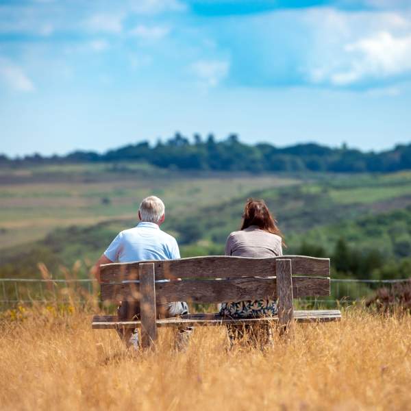 Two people sitting on a bench looking out on the rolling hills and woodland at Ashdown Forest, East Sussex