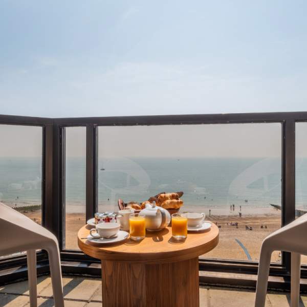 a balcony room at The View hotel in Eastbourne. There is a breakfast on the table, two chairs and a view over the sea and beach