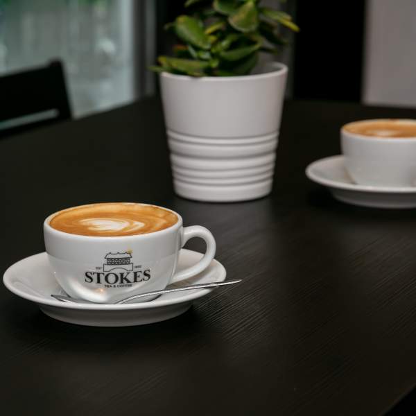 Stokes coffee mug with coffee on table with plant in background