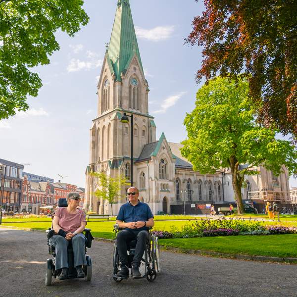 To mennesker i rullestol foran Domkirken i Kristiansand