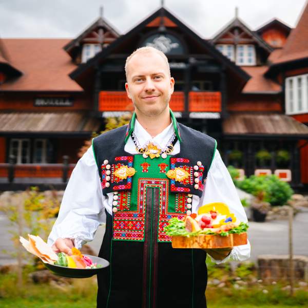 Mann i bunad holder fat med tradisjonell mat foran Sølvgarden hotell