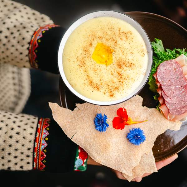 Person i bunad holder en skål med rømmegrøt, spekemat og flatbrød