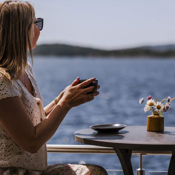Kvinne sitter på bord ute og ser utover havet