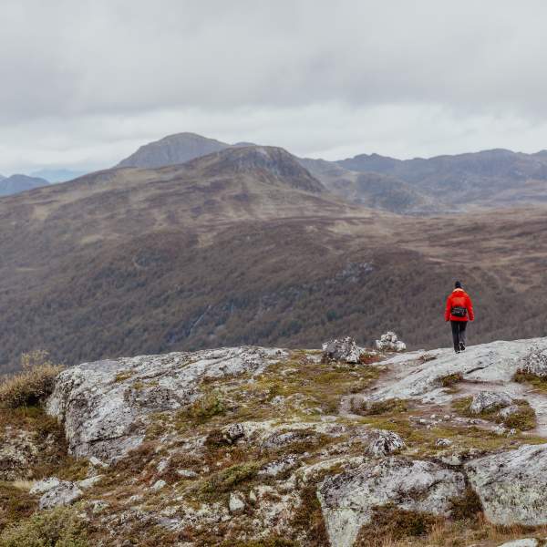 Kvinne i rød jakke på Hovdenuten i Hovden med fjell i bakgrunnen