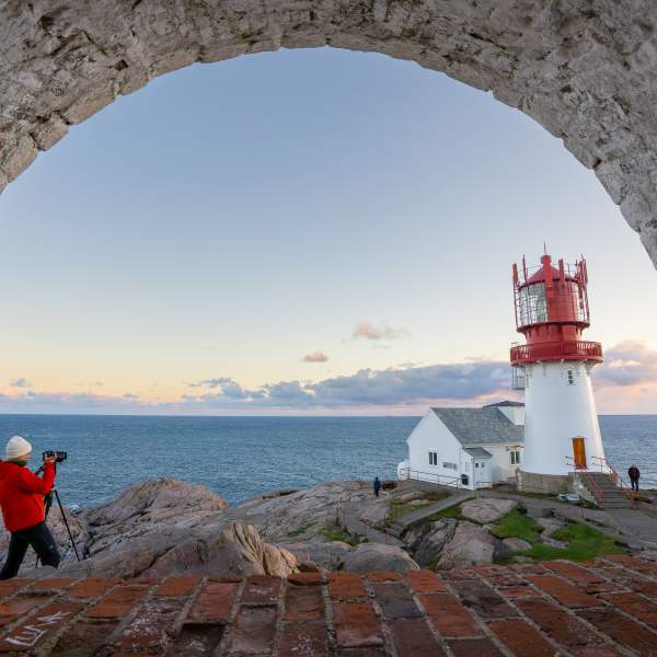 Kvinne i orange jakke fotograferer Lindesnes Fyr