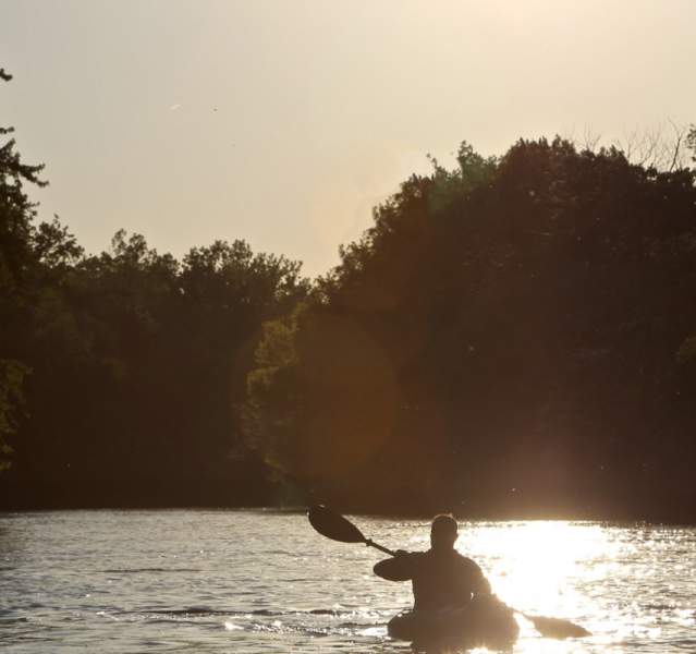 Kayaker paddling the Kankakee river, silhouetted by the sun