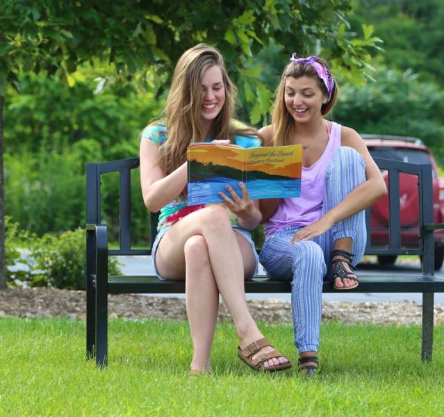 Two women sitting on a bench, reading a visitors guide