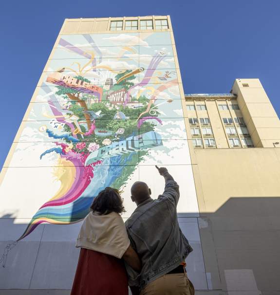 Couple pointing upward at tall, colorful mural
