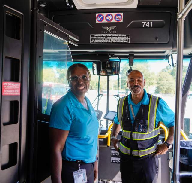 Bus driver and staff member smiling at the front of a motorcoach, welcoming group tour passengers in Fayetteville, North Carolina
