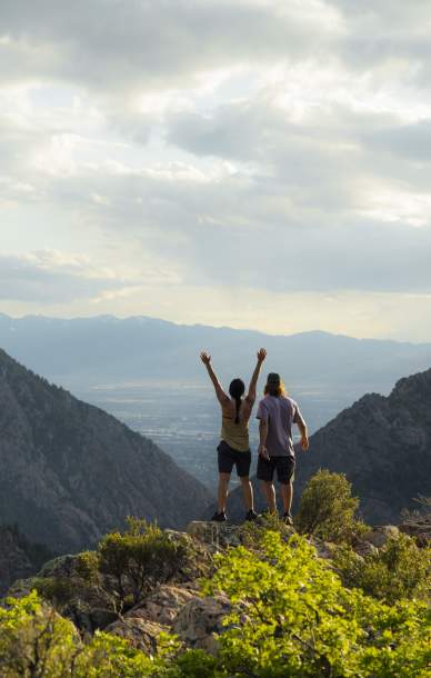 Couple standing on a rock with arms up the view looks down through a canyon into the Salt Lake valley
