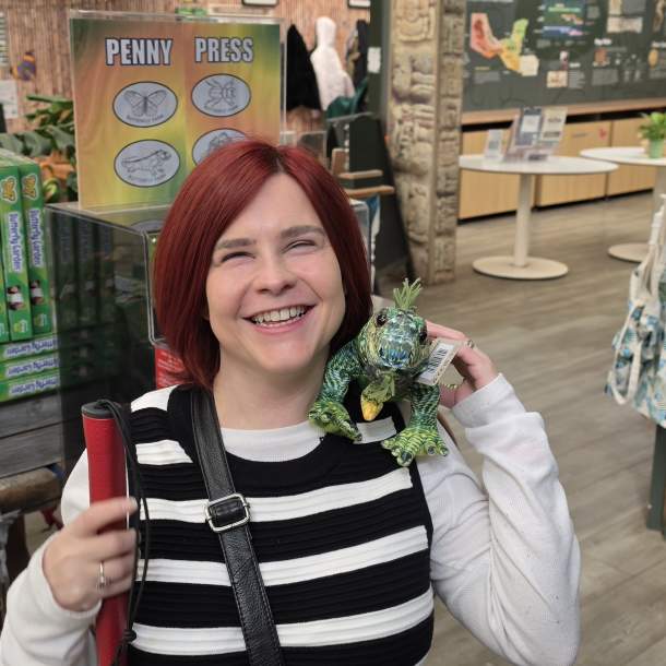 Sassy in the Butterfly Farm gift shop, she has a stuffed iguana on her shoulder smiling towards the camera