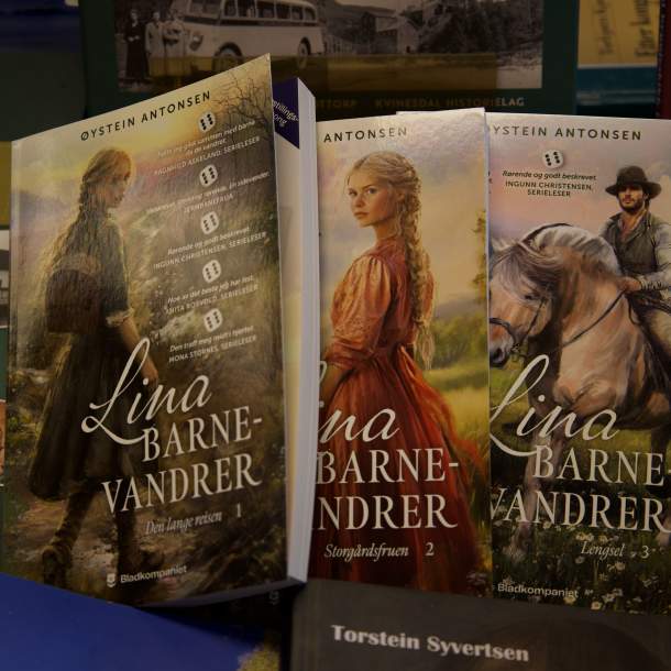 Tre bøker fra serien Lina Barnevandrer av Øystein Antonsen utstilt i Lyngdal Bokhandel, omgitt av lokalhistoriske bøker fra regionen.