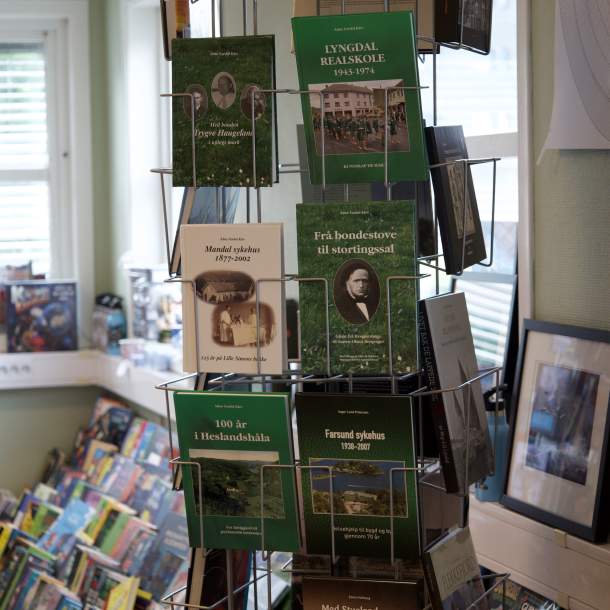 Bokstativ med lokalhistoriske utgivelser som «Lyngdal Realskole», «Frå bondestove til stortingssal» og «Mandal sykehus» utstilt i Lyngdal Bokhandel.