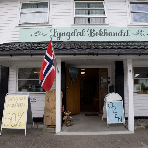 Inngangen til Lyngdal Bokhandel med norsk flagg og skilt utenfor.