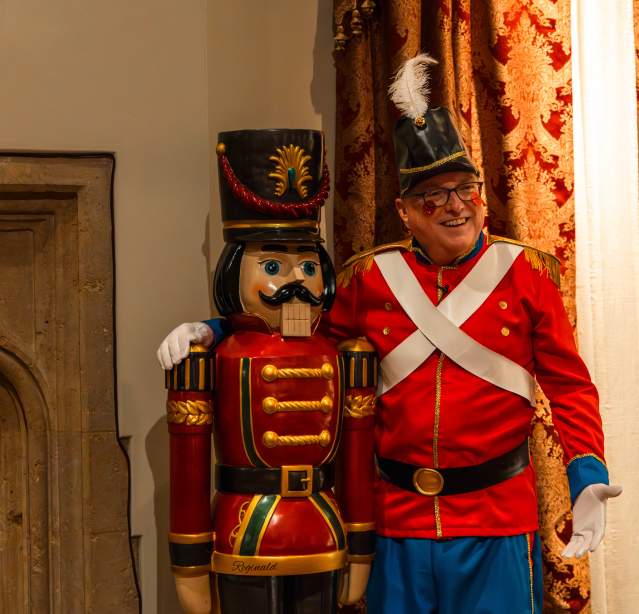 A man dressed as a nutcracker stands in front of a large nutcracker at the Nutcracker in the Castle exhibit at the Paine Art Center