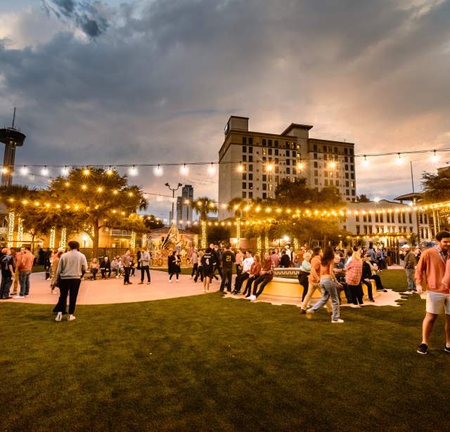 Large outdoor gathering at dusk with decorative lighting