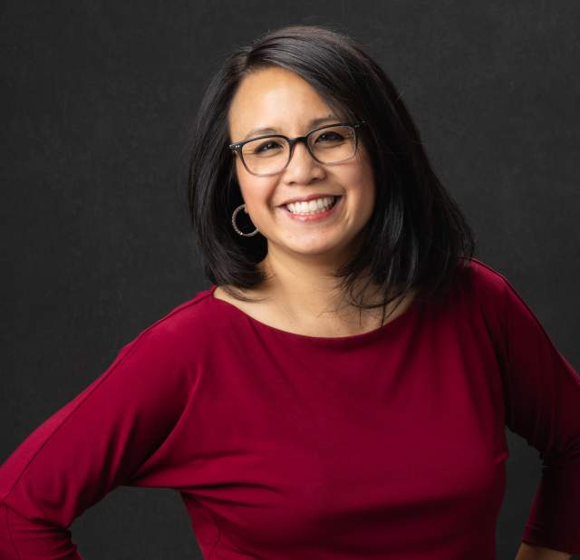 A woman wearing a red blouse smiling into the camera posing for a headshot.