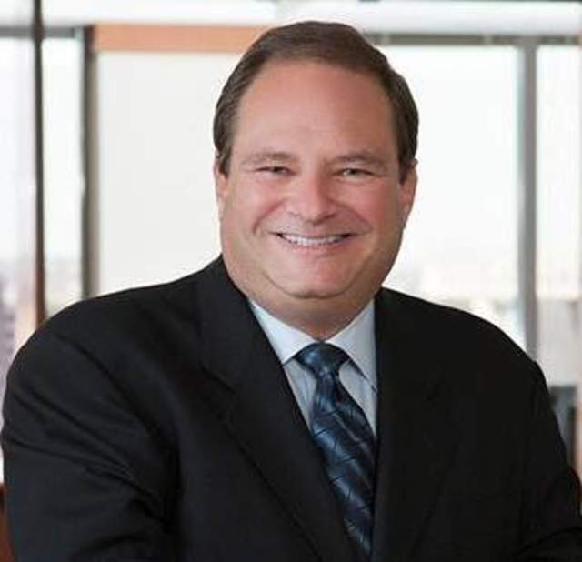 A man wearing a suit and tie smiling into the camera posing for a headshot.